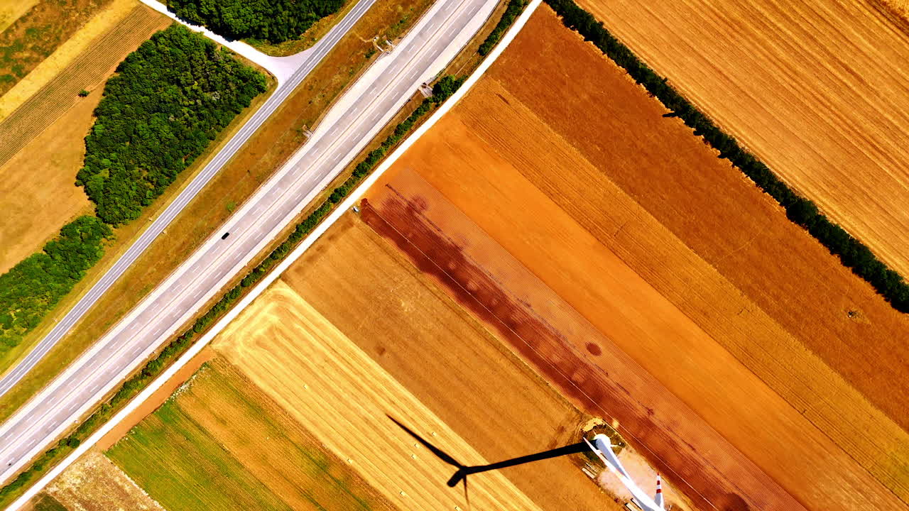 Bright yellow and orange fields with the road nearby. Flight over the wind turbine producing energy