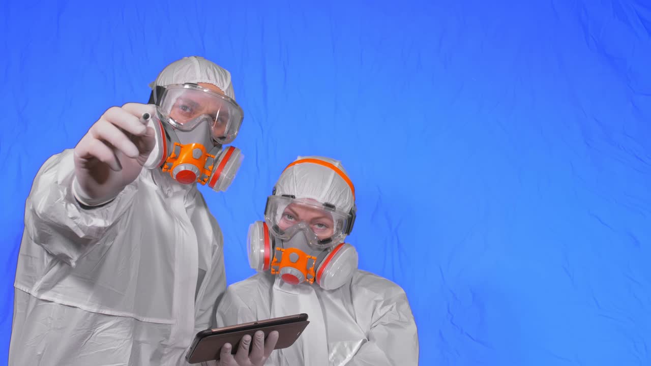 científico virólogo en respirador hace escribir en una tableta con lápiz. hombre y mujer con máscara médica protectora. clave de croma azul.