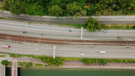 Drohnenaufnahme,-Die-Quer-über-Eine-Stark-Befahrene-Autobahn-Schwenkt,-Mit-Einem-Vorbeifahrenden-Zug-In-Der-Mitte