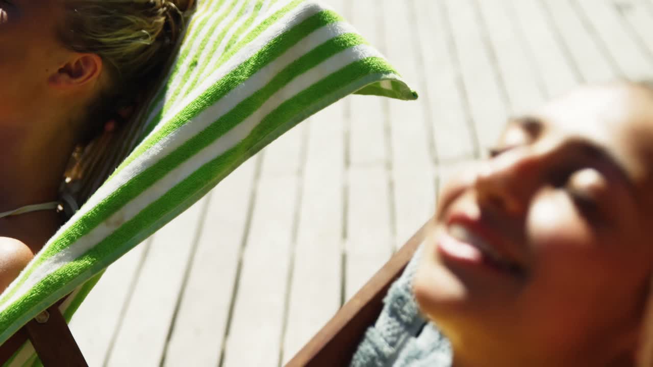 dos mujeres acostadas en sillas de cubierta tomando el sol cerca de la piscina