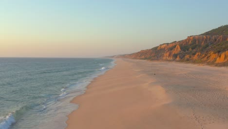 flying through an empty beach, arriba fossil da praia da gale fontainhas seaside cliff rock formation during sunset in the coast shore