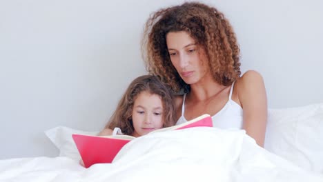 madre enfocada leyendo un libro a su hija