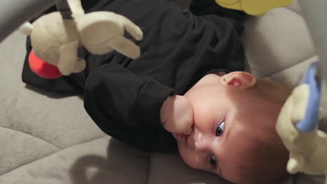 looking down on baby girl on back, chewing on fist, playing with hanging toys