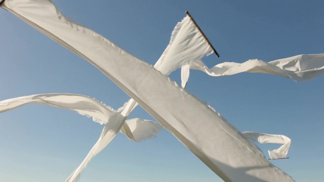 Pannelli di tessuto bianco ondeggianti che rispondono alla brezza, sollevandosi e attraversando il cielo azzurro limpido, con clip.