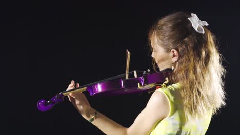 young violinist woman playing violin on dark stage.