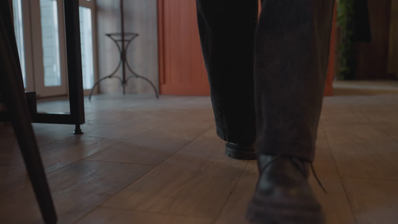 low angle close up of young lady wearing wide leg jeans and black shoes walking through glass restaurant door toward chair, soft daylight from outside