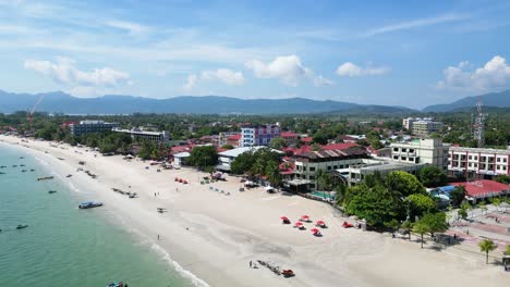 Drone-view-of-Cenang-beach-with-tourists-and-mountains-at-background-on-a-sunny-day-in-Malaysia