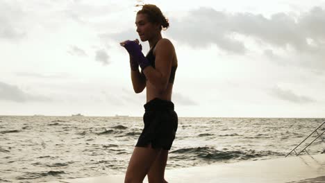 athletic karate woman makes sidekick of her legs against the son by the sea in slow motion. beautiful female boxer training on