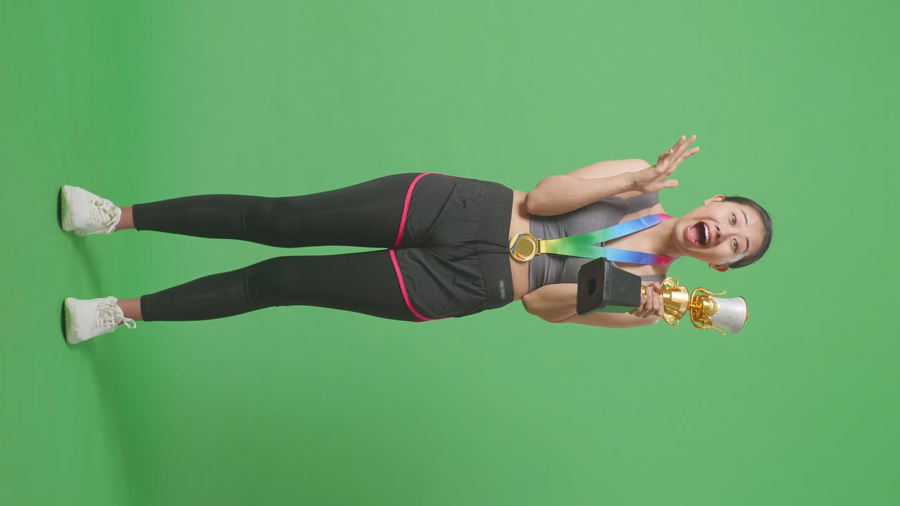cuerpo lleno de mujer asiática con una medalla de oro mirando un trofeo de oro en sus manos y diciendo wow estar feliz ganando como el primer ganador en el fondo de la pantalla verde en el estudio