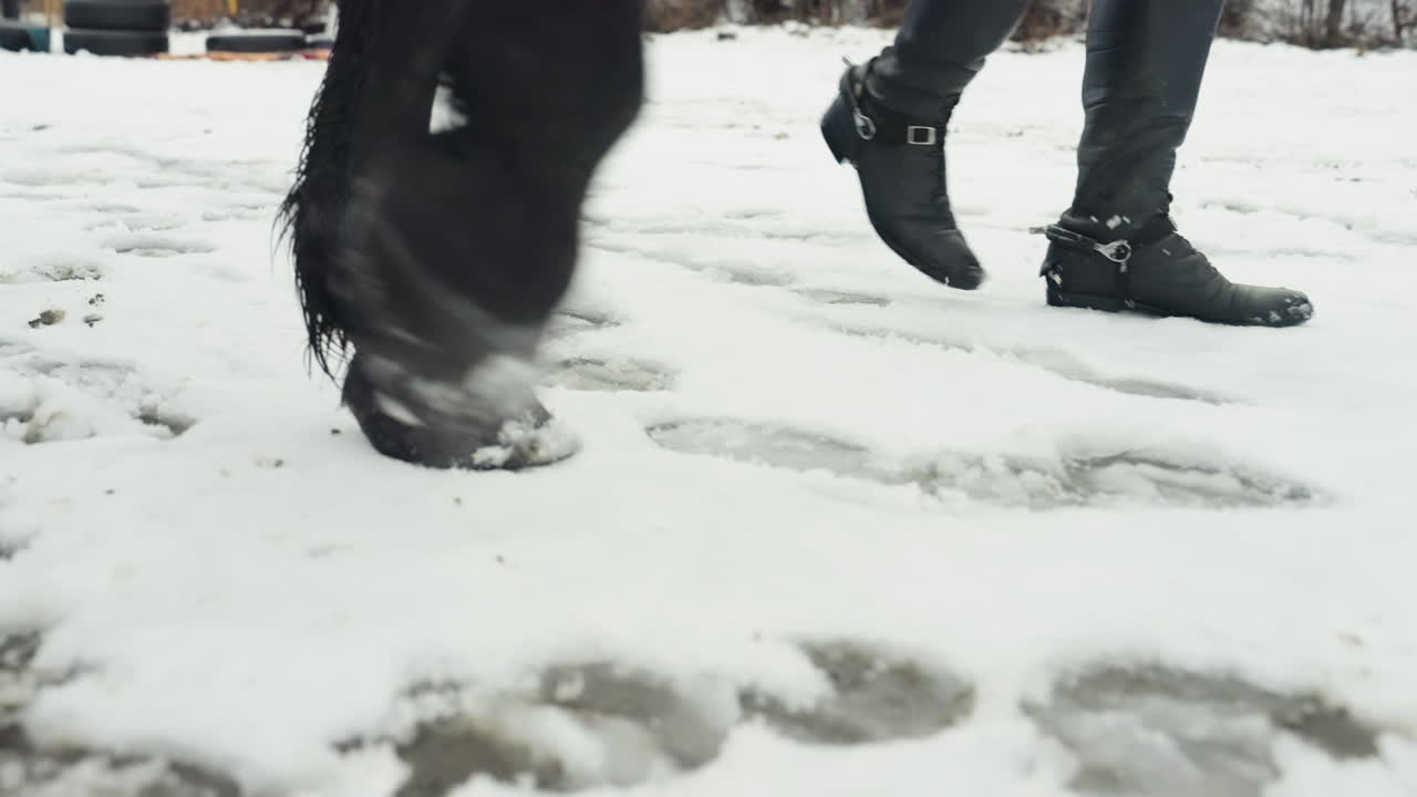 Primer plano de botas y cascos de caballo en la nieve, jinete y caballo caminando por terreno invernal con aguanieve y huellas visibles, tonos fríos apagados, pasos rítmicos y constantes y aguanieve helada texturizada bajo los pies.