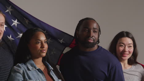 studio portrait shot of multi-cultural group of friends holding american flag behind them celebrating 4th july independence day 2