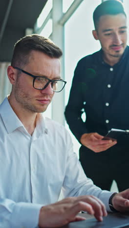 two businessmen working on a laptop in an office