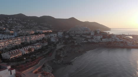 Bay-cityscape-drone-rising-above,-sun-beam-from-right-side,-ocean-and-waves