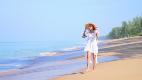 Glückliche-Frau-In-Weißem-Sommerkleid-Und-Strohhut,-Die-Barfuß-Am-Strand-Entlang-Auf-Meeresgezeiten-Geht,-Sonniger-Tag-Am-Strand-Der-Tropischen-Insel