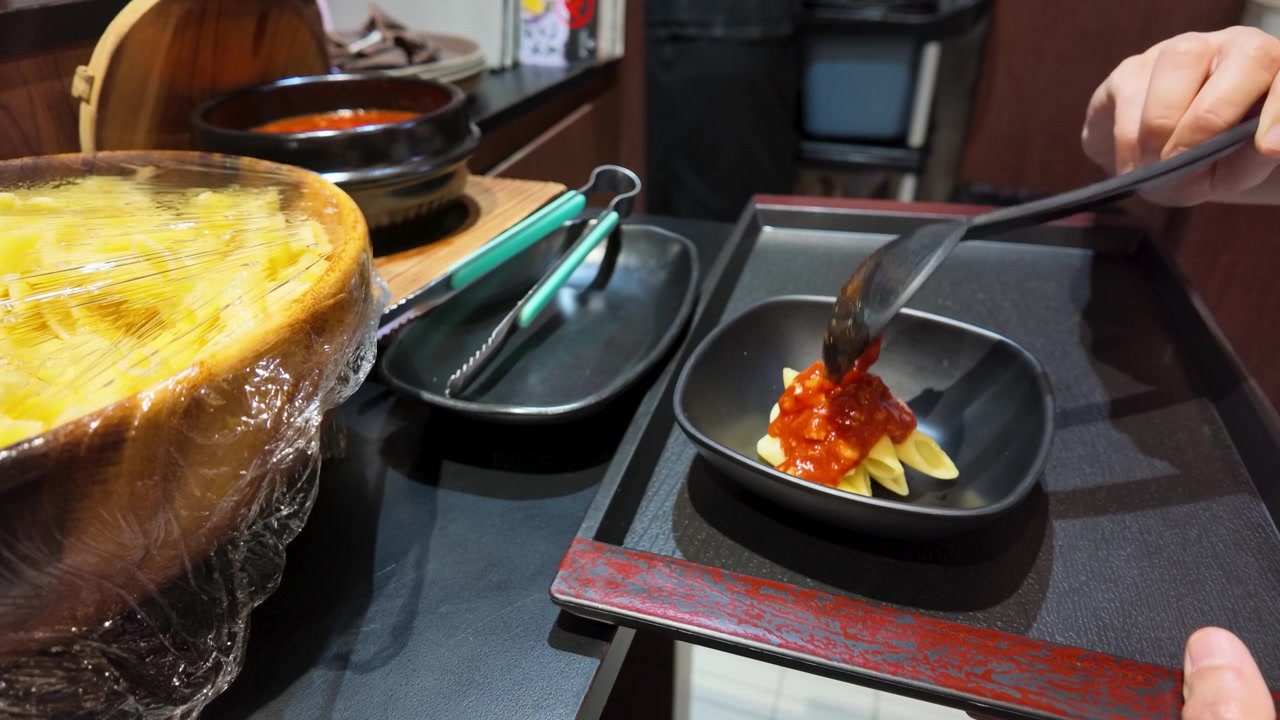 Una persona versa con un mestolo salsa rossa su pasta penne in una piccola ciotola in un ristorante
