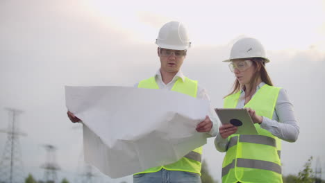 Ingenieure-In-Uniform-Arbeiten-Mit-Einem-Laptop-In-Der-Nähe-Von-Übertragungsleitungen.