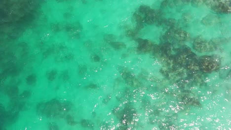 Bird's-eye-view-of-shallow-glinting-turquoise-ocean-with-sand-and-reef