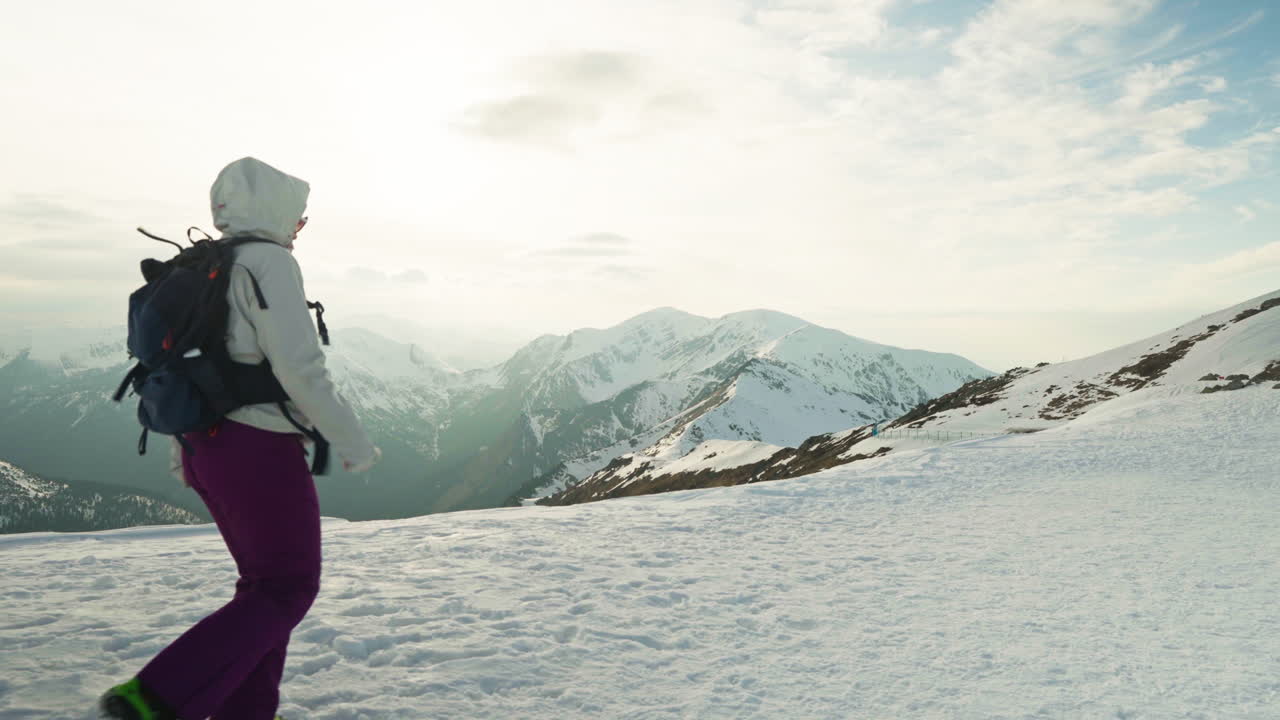 Pan shot of woman on top of snowy mountain hiking and looking at the beautiful landscape, gimbal shot