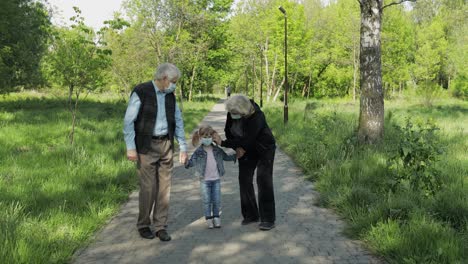 Alte-Großeltern-Mit-Enkelin-In-Medizinischen-Masken-Gehen-Im-Park-Spazieren.-Coronavirus