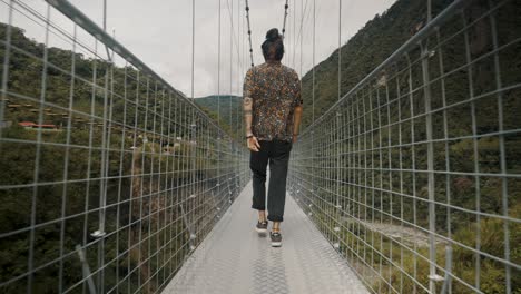 Man-walking-over-a-bridge-during-tour-in-Baños-de-agua-santa,-Ecuador