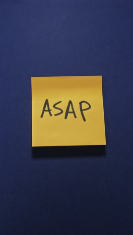 hands posting asap sticky note on dark blue wall, highlighting priority tasks