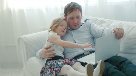 father and daughter using laptop on the sofa