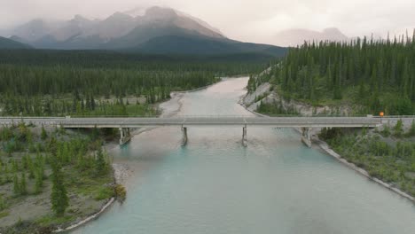 aerial dolly in of road bridge over bow river between pine tree forest, canadian rockies in back at banff national park, alberta, canada