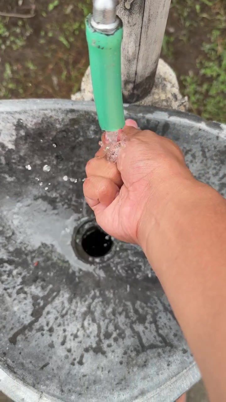Primo piano di una mano che apre e chiude l'acqua da un rubinetto esterno.