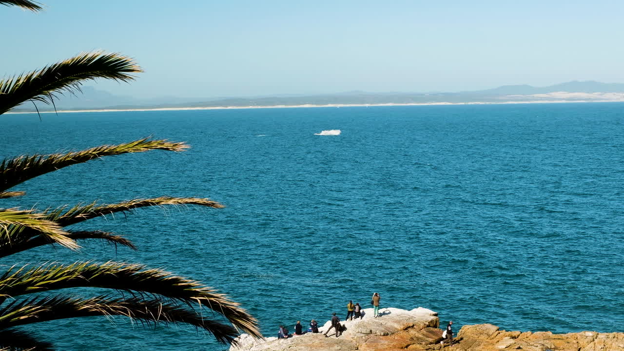 los turistas en hermanus en el mirador costero rocoso observan una brecha de ballenas en walker bay - temporada de ballenas, sudáfrica