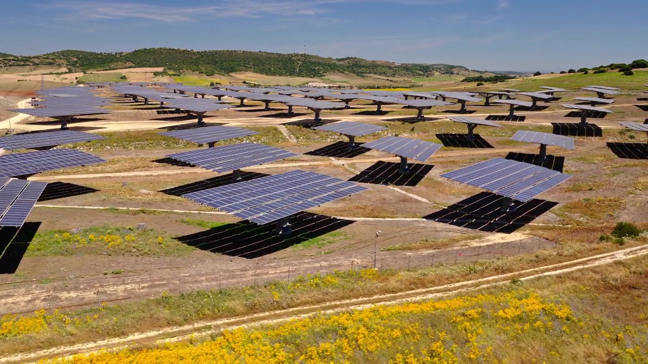 Filmato cinematografico con drone che sorvola un grande impianto fotovoltaico con pannelli che generano elettricità pulita e rinnovabile. Infrastruttura energetica sostenibile a supporto della transizione energetica globale.