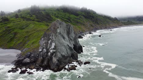 4k 30fps aerial footage oregon coast - flying in the clouds, waves crashing against the rocky moss shore, turquoise blue water diamond shaped rock pacific ocean shore in south oregon - dji drone video