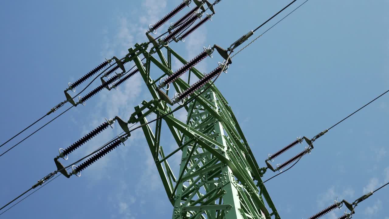 High voltage power lines and pylon, low angle shot with blue sky in the background - sliding left