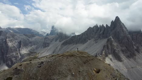 Un-Dron-De-Rotación-Aérea-De-Un-Excursionista-Parado-Solo-En-Un-Acantilado-Con-Las-Impresionantes-Montañas-De-Los-Dolomitas-Rodeándolo