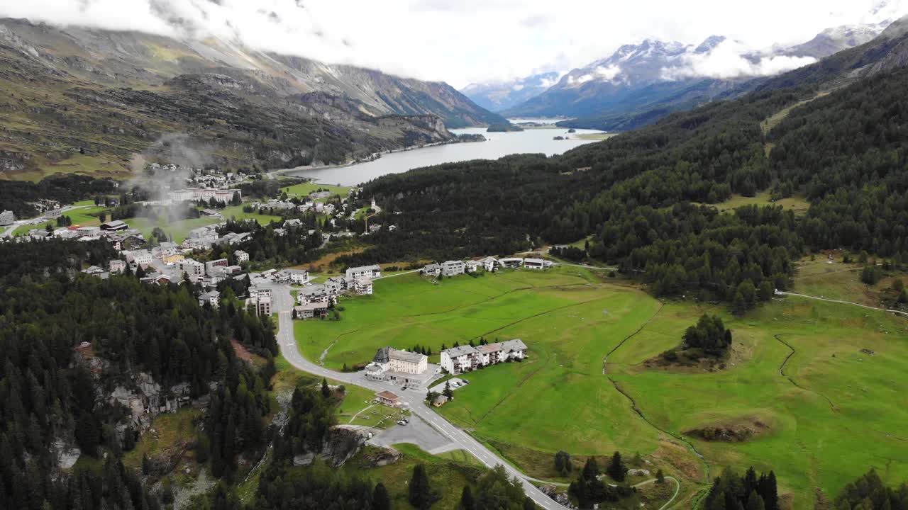 sobrevuelo aéreo con vista panorámica desde el lago sils hasta los giros del paso de maloja en engadin, suiza con autos que suben y bajan por la carretera rodeada de árboles