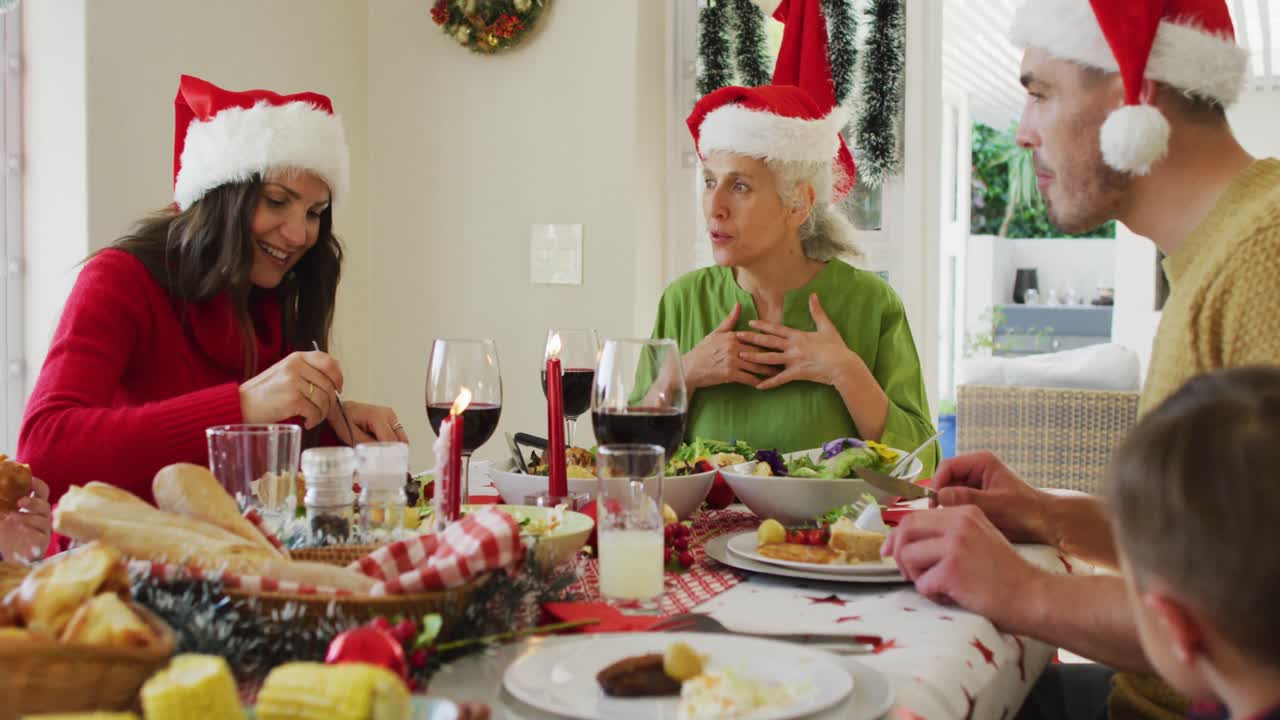 familia caucásica feliz de varias generaciones con sombreros de papá noel, teniendo la comida de navidad