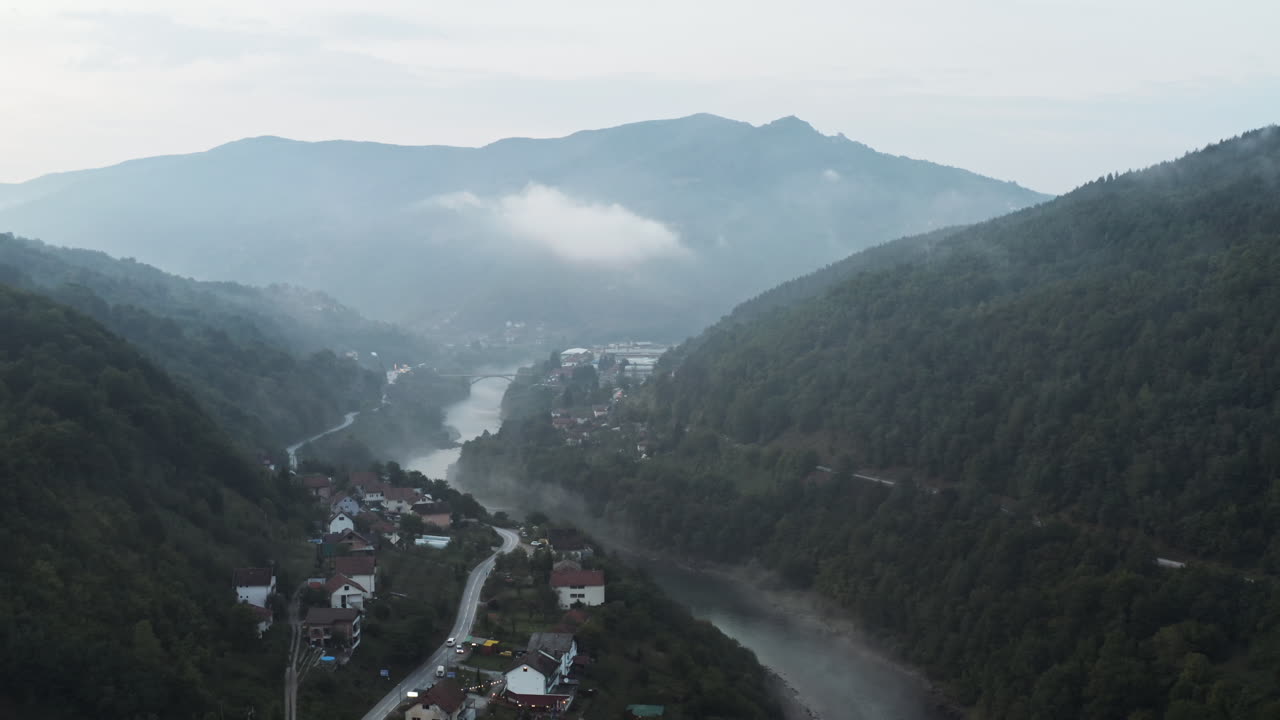 volando sobre un pueblo en los balcanes por un río con nubes bajas soñador