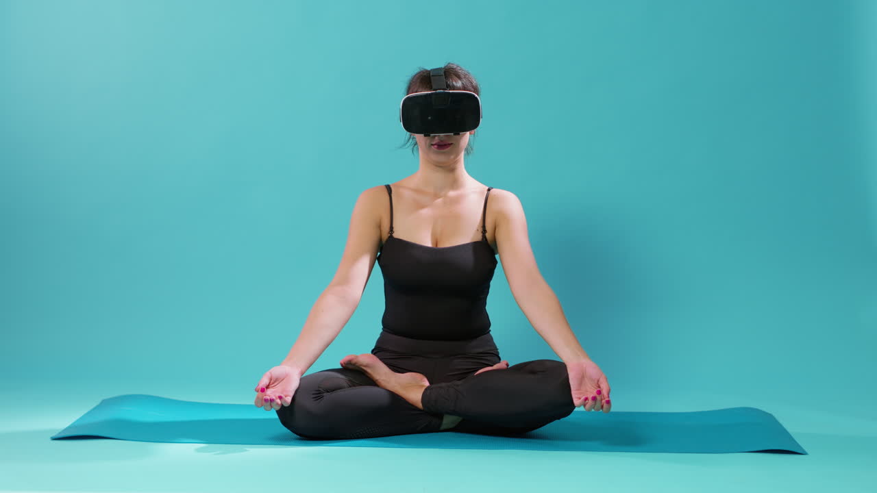 Mulher sentada em posição de lótus com óculos de realidade virtual em um colchonete de yoga