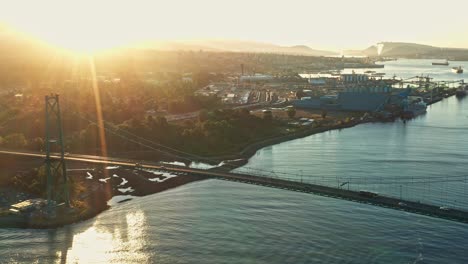 drone tilt aerial shot with the sun peaking over the lions gate bridge in front of vancouver harbour