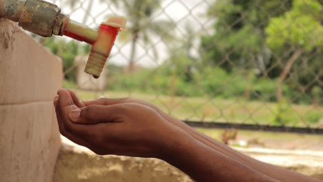 concept of water conservation, public water tank tap water drops falling into the hands in india