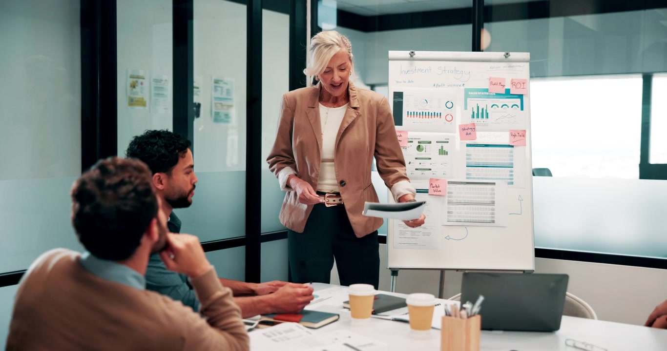Empresaria madura dirigiendo una reunión de estrategia en una oficina moderna.