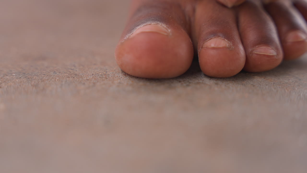 Primo piano delle dita dei piedi che premono sulla sabbia, piccole dita dei piedi che si muovono sui granelli, esplorazione tattile sul bagnasciuga, luce calda e soffusa, attenzione al letto ungueale e alla texture della pelle, momento ludico di radicamento.