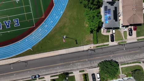 una vista de arriba hacia abajo de la bandera estadounidense que sopla en el viento en el campo deportivo de una escuela en un día soleado