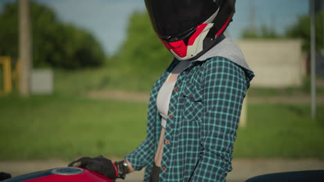 a close-up of a female rider standing next to her power bike, she is wearing canvas shoes and black sports trousers, holding the bike with her right hand as it rests on the ground