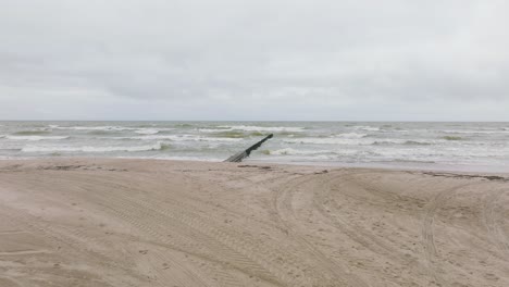 Estableciendo-Una-Vista-Aérea-De-La-Costa-Del-Mar-Báltico-En-Un-Día-Nublado,-Un-Viejo-Muelle-De-Madera,-Una-Playa-De-Arena-Blanca,-Grandes-Olas-De-Tormenta-Aplastando-La-Costa,-Cambios-Climáticos,-Un-Amplio-Tiro-De-Drones-Avanzando-Bajo