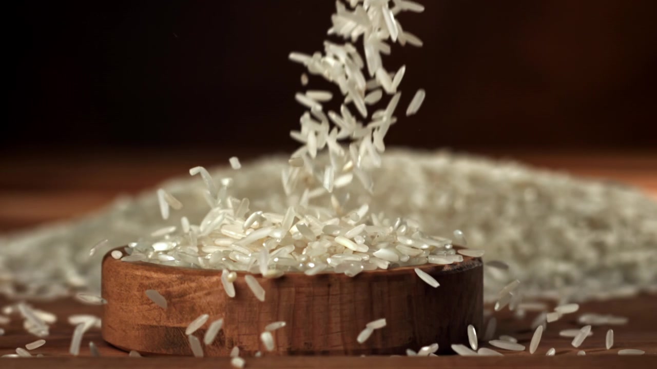 Hvide ris falder ned i en træskål i slowmotion