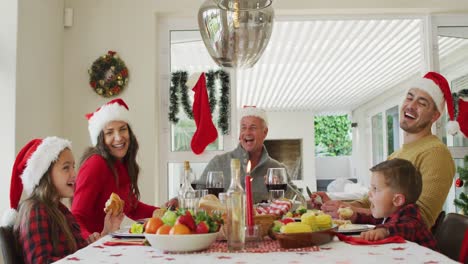 Feliz-Familia-Caucásica-Multigeneración-Con-Gorros-De-Papá-Noel,-Comiendo-Navidad