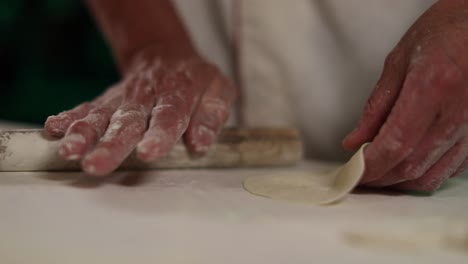 professional chef using a small roller to flatten dumpling dough