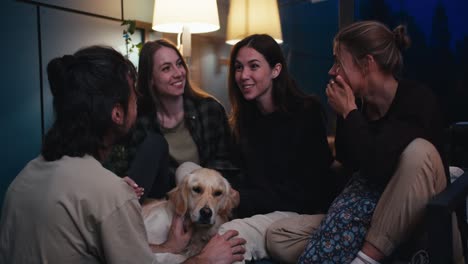 Un-Grupo-Feliz-De-Amigos,-3-Chicas-Y-Un-Chico-Están-Hablando-Cerca-De-Ellos-Y-Su-Perro-Tiene-Colores-Claros-En-Una-Acogedora-Habitación-Por-La-Noche.