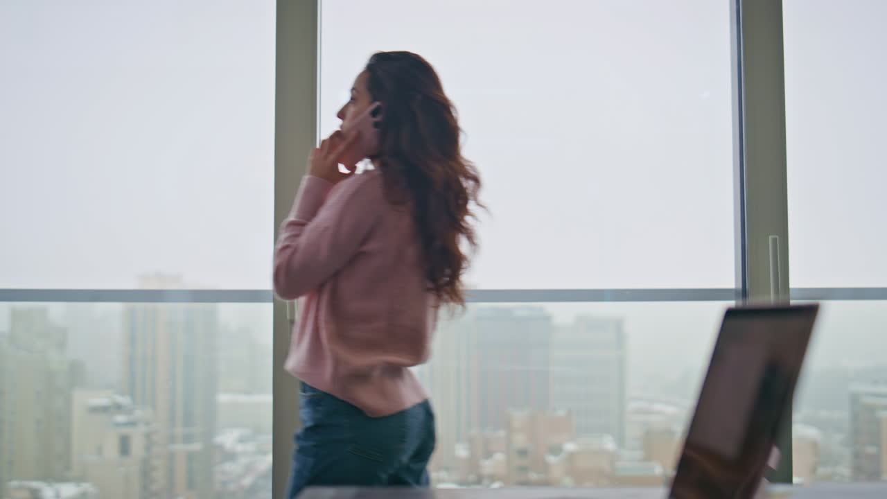 젊은 사업가 여성이 스마트폰으로 전화하고 파노라마 창문에서 걸어가고 있습니다.