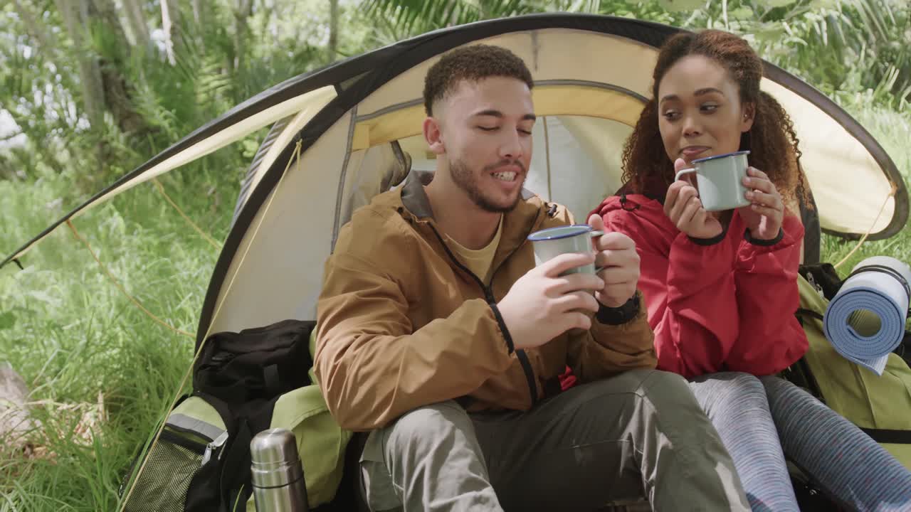 Felice coppia afroamericana in campeggio che beve caffè nel bosco, al rallentatore